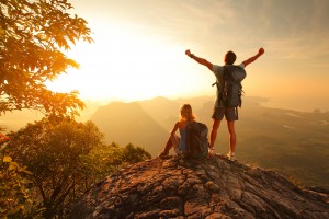 Two hikers enjoying sunrise from top of a mountain